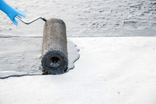 Roofer worker painting bitumen praimer at concrete surface by the roller brush, Â for waterproofing