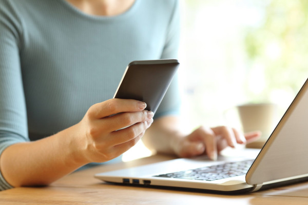 Close up of a girl hands using a smart phone and a laptop on a desk at home